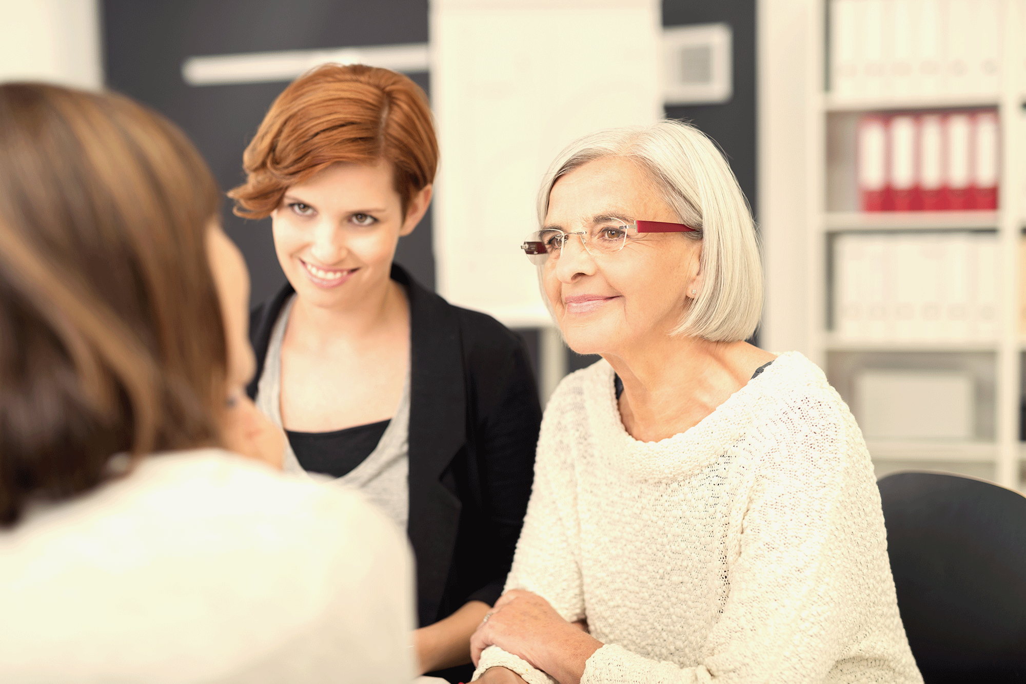 A woman sits in a chair and listens attentively to others in an example of empathetic leadership.