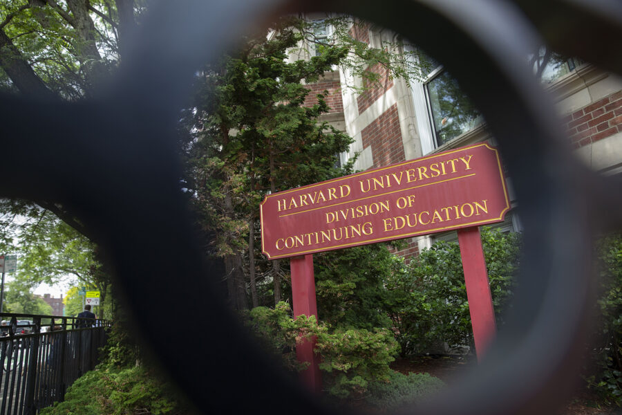 A sign for the Division of Continuing Education seen through a piece of fence.