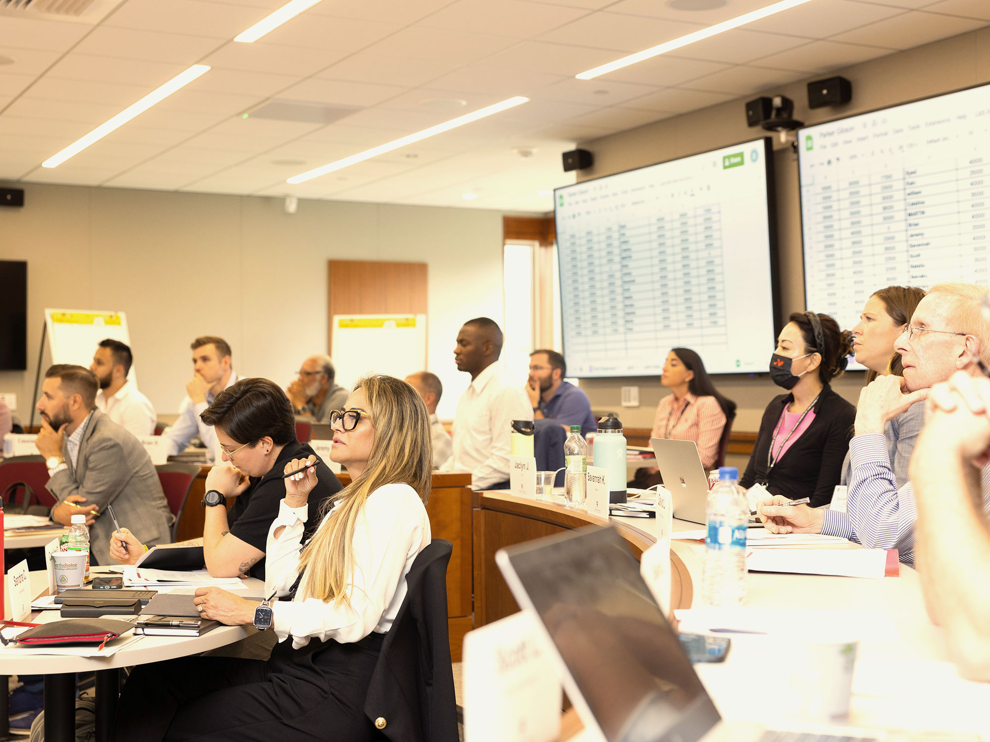 Participants focused on a classroom lecture with spreadsheets displayed on dual screens.