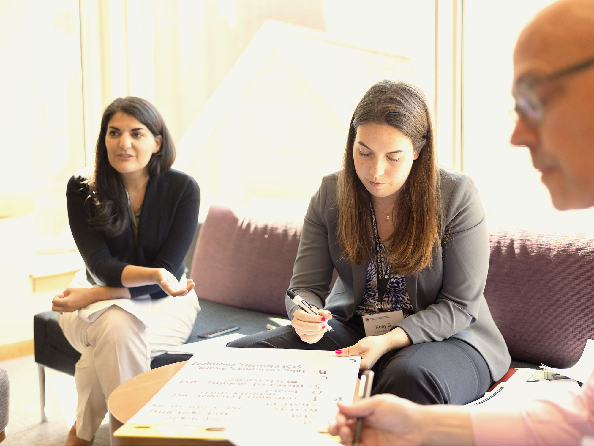 Three participants sit together, writing and sharing ideas in a bright room.