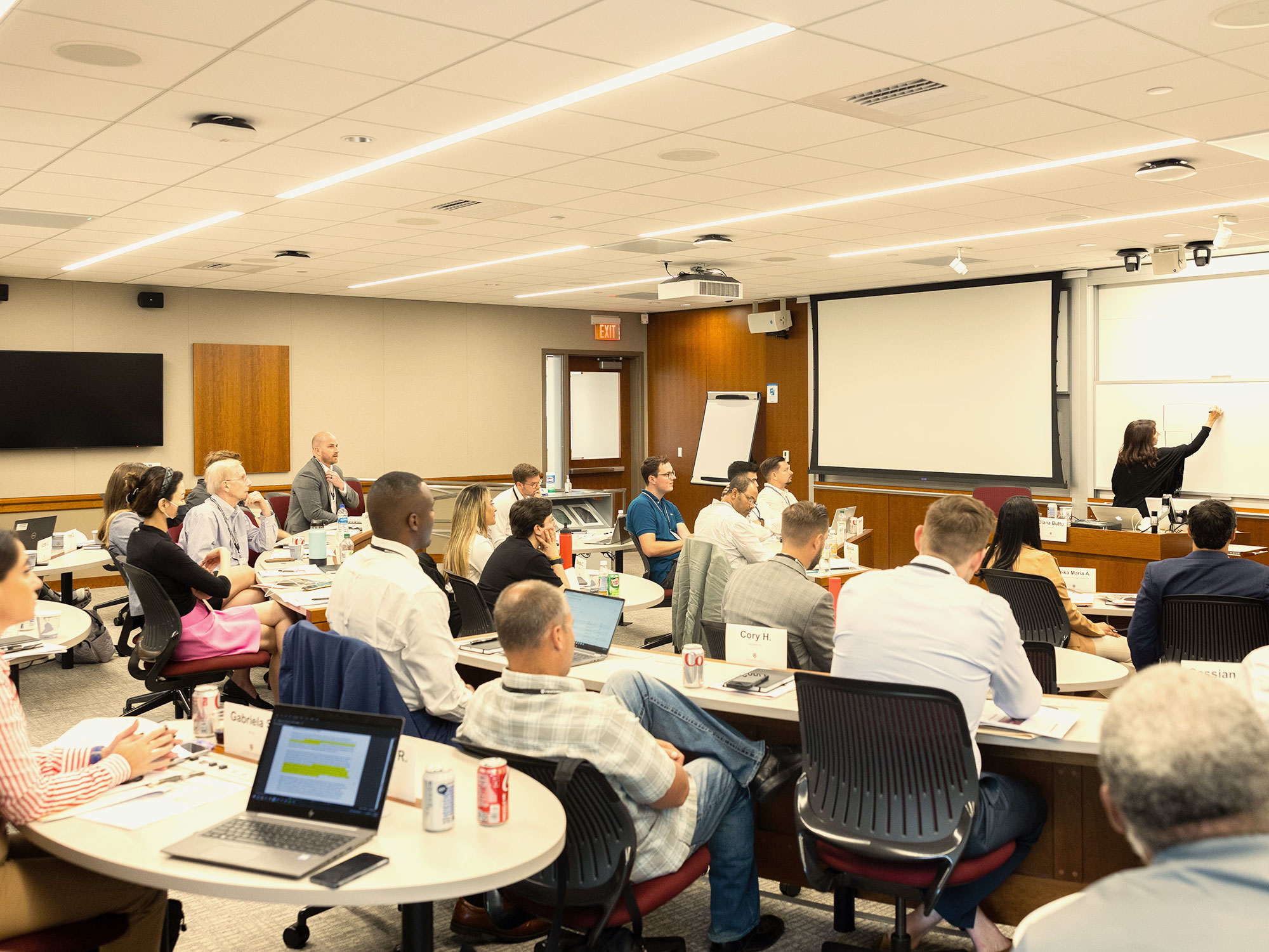A full classroom watches a presenter at the whiteboard.